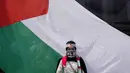 Seorang perempuan berdiri di depan bendera besar Palestina saat aksi bela Palestina, di Monumen Nasional atau Monas, Jakarta Pusat, Minggu (5/11/2023). (AP Photo/Dita Alangkara)