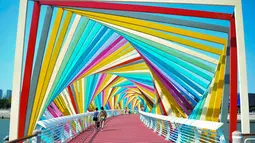Warga berjalan melintasi jembatan warna-warni seperti pelangi yang berada di Qingdao, Shandong, China, Kamis (6/9). Jembatan pelangi ini terletak di Tangdaowan Seaside Park. (STR/AFP)