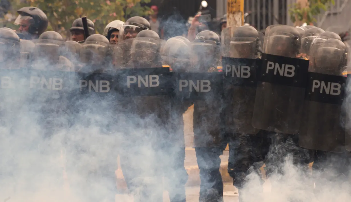 Polisi antihuru-hara berlindung dari serangan gas air mata mahasiswa Venezuela Central University, Caracas, Venezuela (21/11). Mereka Menuntut peningkatan anggaran beasiswa dan membuka kembali kafetaria universitas. (AP Photo/Ariana Cubillos)