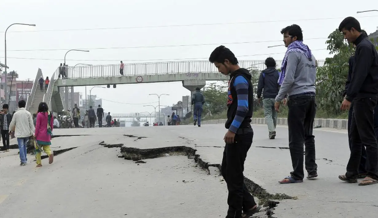 Sejumlah warga di Kathmandu berjalan melintasi jalan yang rusak akibat gempa, Minggu (26/4/2015). Gempa berkekuatan 7,8 Skala Richter dikabarkan telah menelan korban sekitar 2000 jiwa. (AFP Photo/Prakash Mathema)