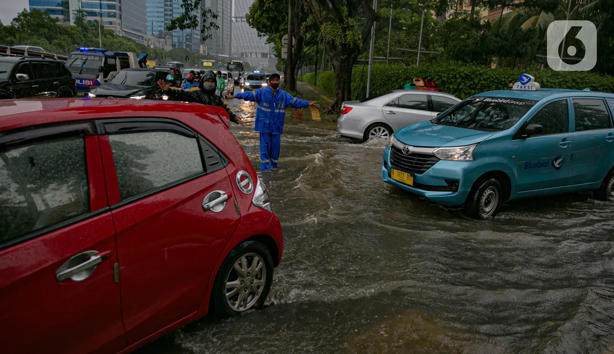 Petugas mengatur kelancaran lalu lintas saat air menggenangi ruas Jalan Gatot Subroto, Jakarta, Kamis (18/2/2021). Hujan deras yang mengguyur wilayah Jakarta menyebabkan terjadinya genangan di beberapa ruas jalan, meski begitu sejauh ini kendaraan masih dapat melintas. (Liputan6.com/Faizal Fanani)