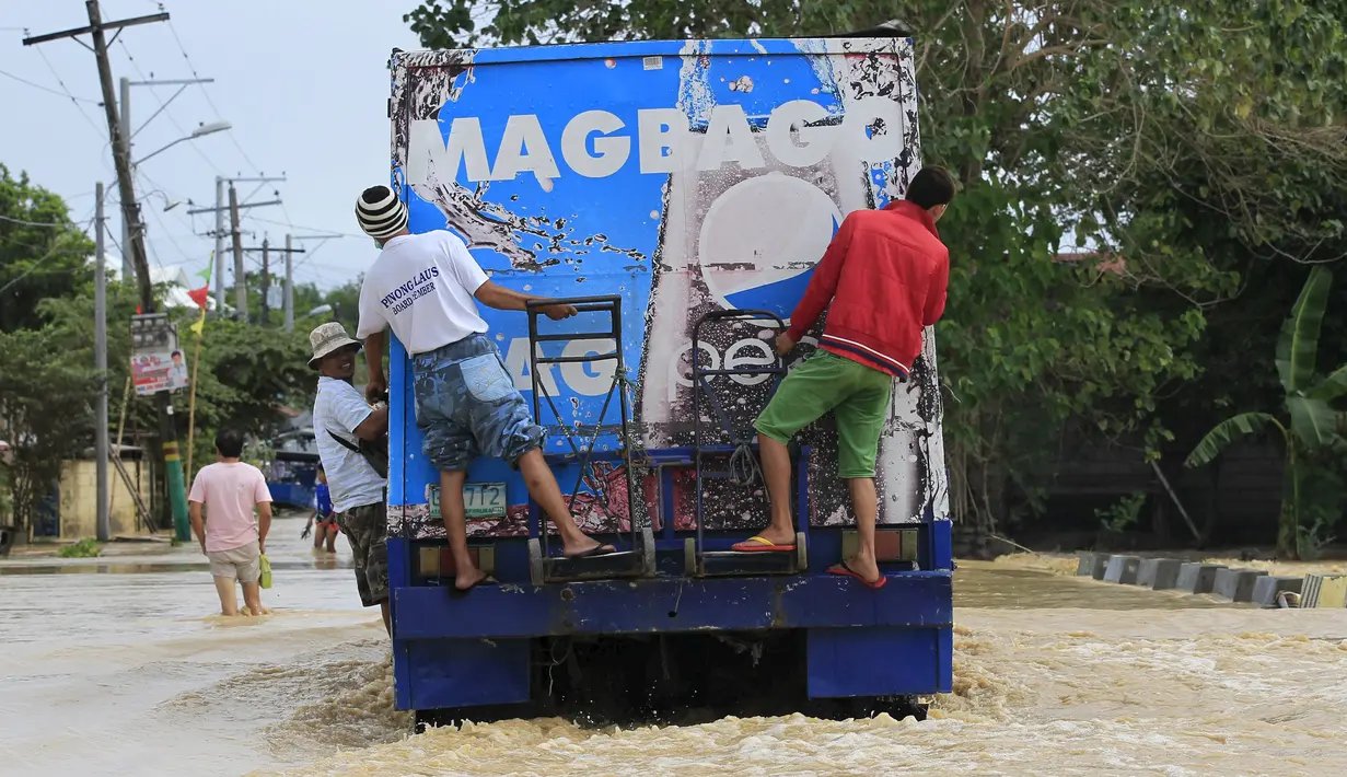 Warga menaiki dibagian belakang truk pengiriman untuk menyeberang banjir setelah hujan lebat di Kota Candaba, Filipina (17/12). Ratusan orang mengungsi di atap rumah mereka akibat banjir yang disebabkan topan beberapa hari lalu. (REUTERS/Romeo Ranoco)