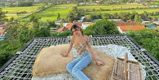 Berpose dengan latar pemandangan sawah, gunung, dan langit yang luar biasa indah, Belleza terlihat mengenakan crop top dengan tali spageti, dipadunya dengan celana jeans panjang. Foto: Instagram.