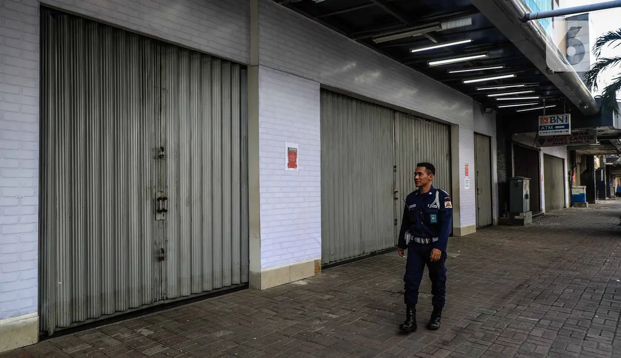 Petugas keamanan berjalan di depan pertokoan kawasan perdagangan Pasar Baru yang tutup, Jakarta, Jumat (3/4/2020). Sebagian pemilik toko di Pasar Baru memilih menutup usahanya sementara waktu untuk mengantisipasi meluasnya penyebaran virus corona COVID-19. (Liputan6.com/Faizal Fanani)
