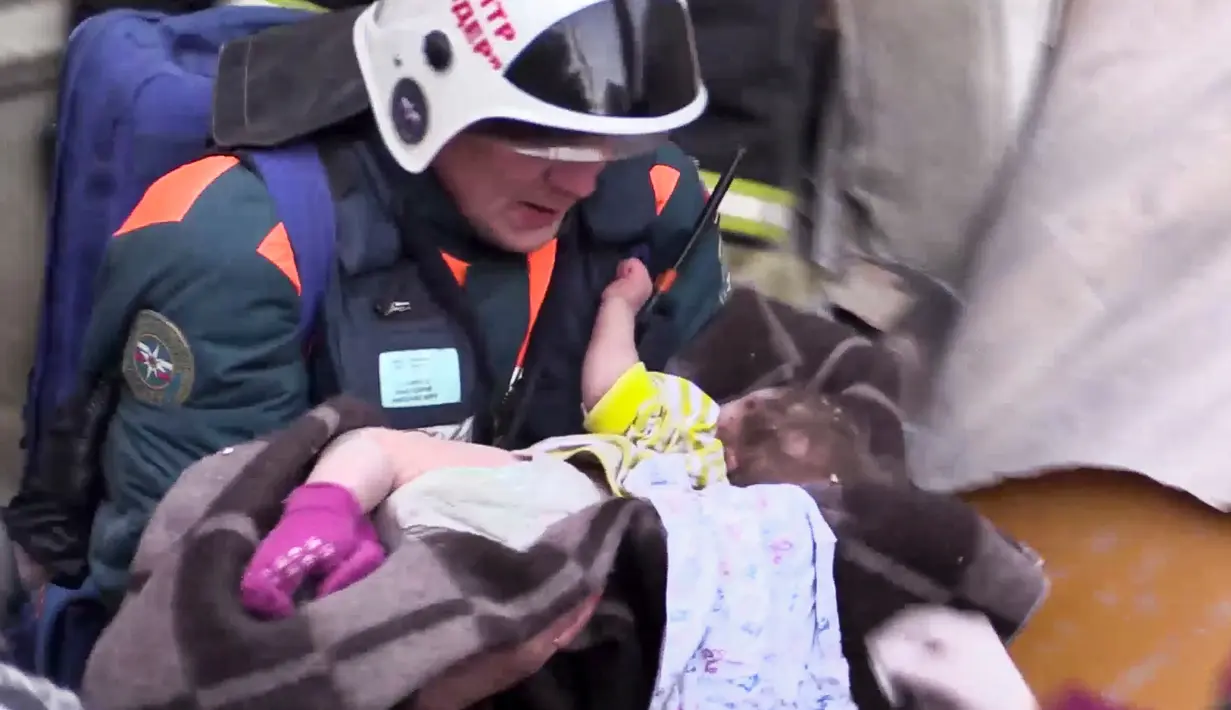 Tim penyelamat menggendong seorang bayi yang ditemukan selamat setelah tertimbun reruntuhan gedung apartemen yang ambruk di Magnitogorsk, Rusia, Selasa (1/1). Bangunan itu porak poranda akibat ledakan gas (Russian Ministry for Emergency Situations via AP)