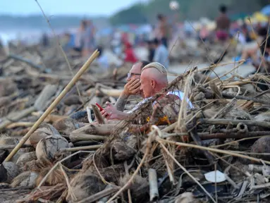 Wisatawan mancanegara duduk di dekat sampah yang terdampar akibat cuaca buruk di Pantai Kuta, Bali, Jumat (15/2). Sampah bervolume besar kembali menepi di Pantai Kuta, kali ini pesisir pantai dipenuhi sampah buah kelapa. (SONNY TUMBELAKA/AFP)