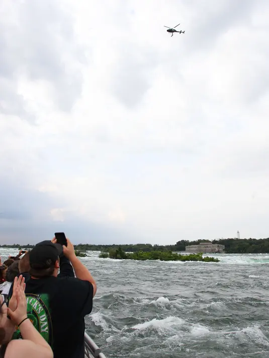 Penonton menyaksikan serangkaian aksi akrobatik yang dilakukan Erendira Wallenda di atas air terjun Niagara, New York, Kamis (15/6). Erendira bergelayutan di lingkaran besi yang dikaitkan pada sebuah helikopter menggunakan giginya. (AP Photo/Bill Wippert)