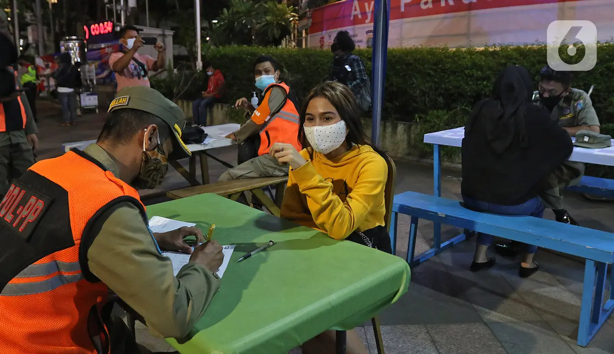 Petugas gabungan mendata pemuda pemudi yang terjaring patroli penegakan protokol kesehatan COVID-19 di bawa ke pos polisi bundaran HI, Jakarta Pusat, Sabtu (26/12/2020). Operasi gabungan itu dilakukan menyusul meningkatnya penyebaran COVID-19 di Ibu kota. (Liputan6.com/Herman Zakharia)