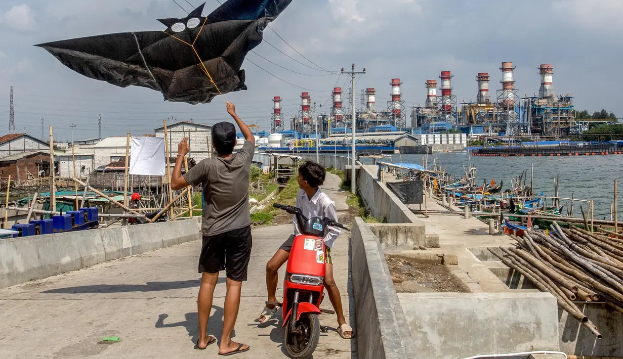 Anak-anak menerbangkan layang-layang saat bermain di sepanjang tanggul laut yang dibangun di desa pesisir Tambaklorok, di Semarang, Jawa Tengah, pada 17 Juni 2025. (DEVI RAHMAN/AFP)