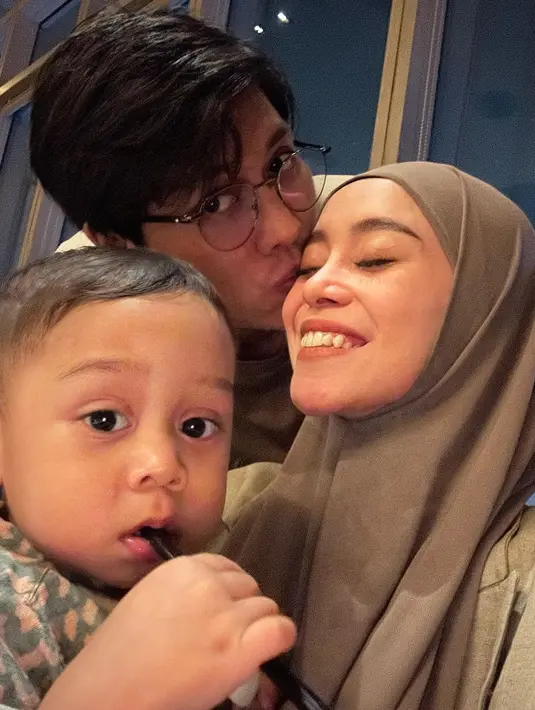 Rizky Billar tampak mencium Lesti dengan penuh kasih sayang. Sementara itu sang bocah sibuk menatap kamera. [Instagram/lestikejora]