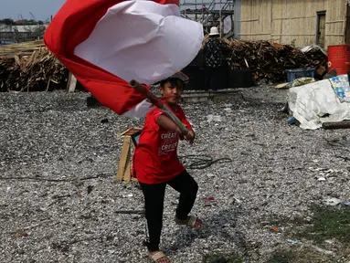 Seorang anak mengibar-ngibarkan bendera Merah Putih usai pelaksanaan Upacara Peringatan HUT RI ke-77 di Kawasan Kalibaru Barat, Cilincing, Jakarta, Rabu (17/8/2022). Memperingati Hari Kemerdekaan Indonesia ke-77, anak-anak yang tergabung dalam Kelas Jurnalis Cilik bersama para relawan melaksanakan upacara bendera dan beragam lomba. (Liputan6.com/Helmi Fithriansyah)