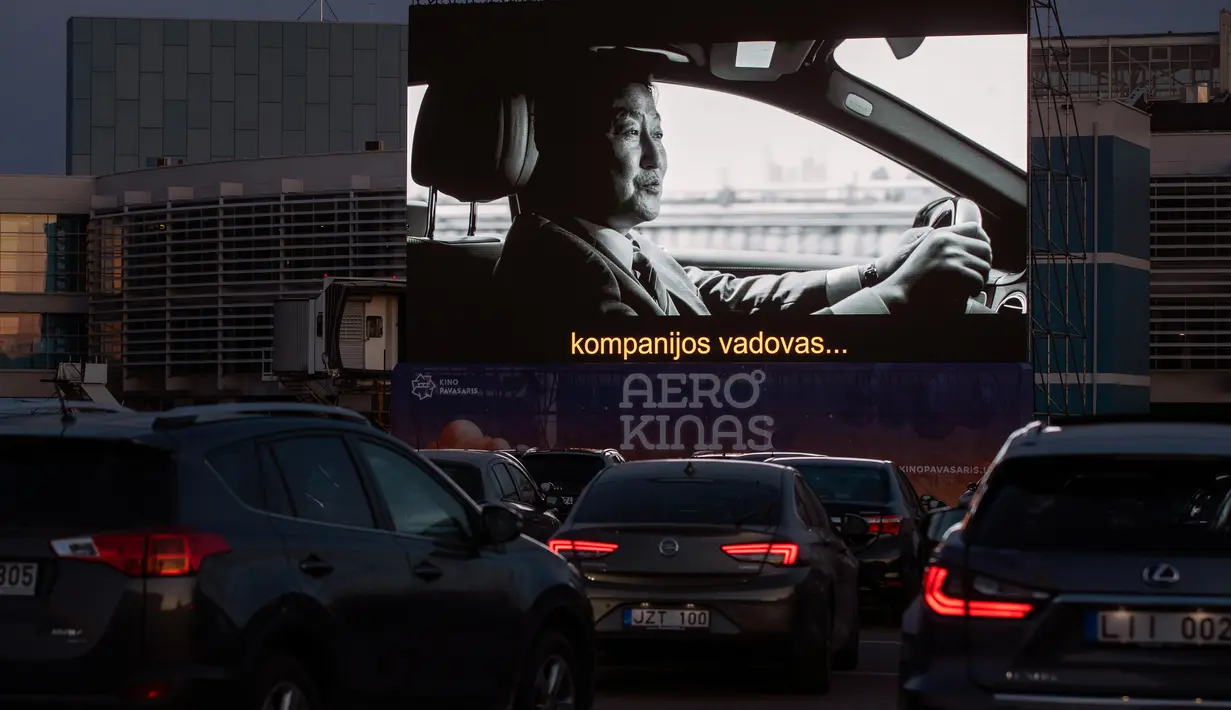 Orang-orang duduk di mobil mereka saat menonton film di bioskop drive-in di area apron bandara kota Vilnius, Lithuania, 29 April 2020. Untuk pertama kalinya dalam sejarah bandara Vilnius mengadakan bioskop drive-in yang beroperasi di tempat pesawat lepas landas dan mendarat. (AP/Mindaugas Kulbis)