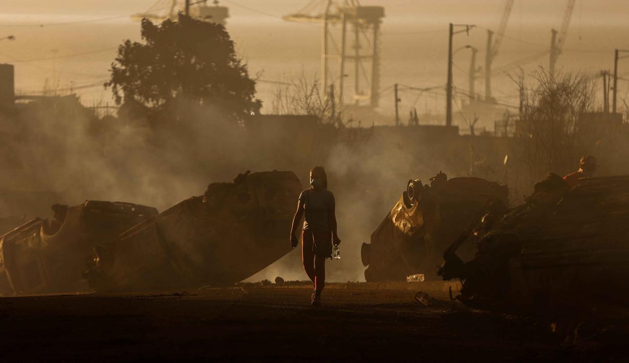 Seorang wanita berjalan di antara mobil-mobil yang hangus terbakar setelah kebakaran hutan di Concepcion, Chile pada 18 Januari 2026. Sedikitnya 18 orang tewas dan puluhan ribu lainnya terpaksa mengungsi akibat kebakaran hutan hebat yang melanda wilayah tengah dan selatan Chile. (Raul BRAVO/AFP)