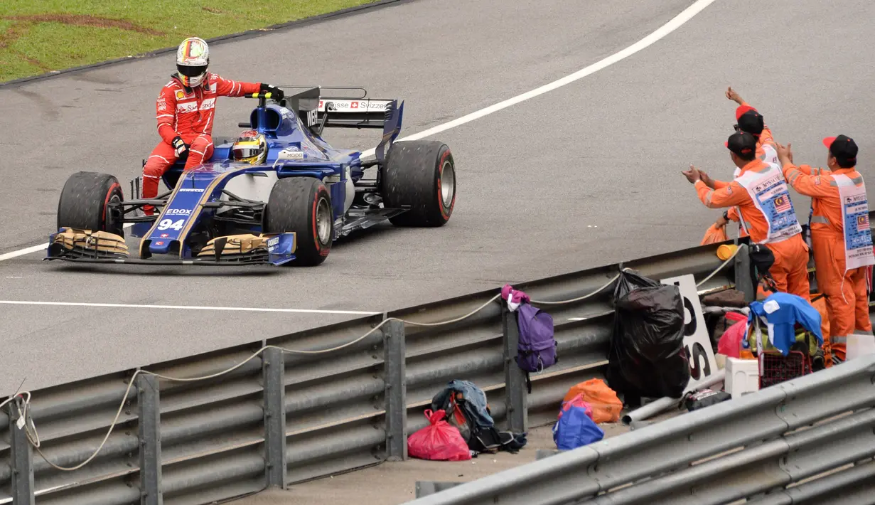 Pebalap Ferrari, Sebastian Vettel mendapat dukungan dari petugas lintasan saat menumpang mobil Pascal Wehrlein pada balapan Formula One Malaysia Grand Prix, Sepang, (01/10/2017). Vettel akhirnya finis pada posisi keempat. (AFP/Roslan Rahman)