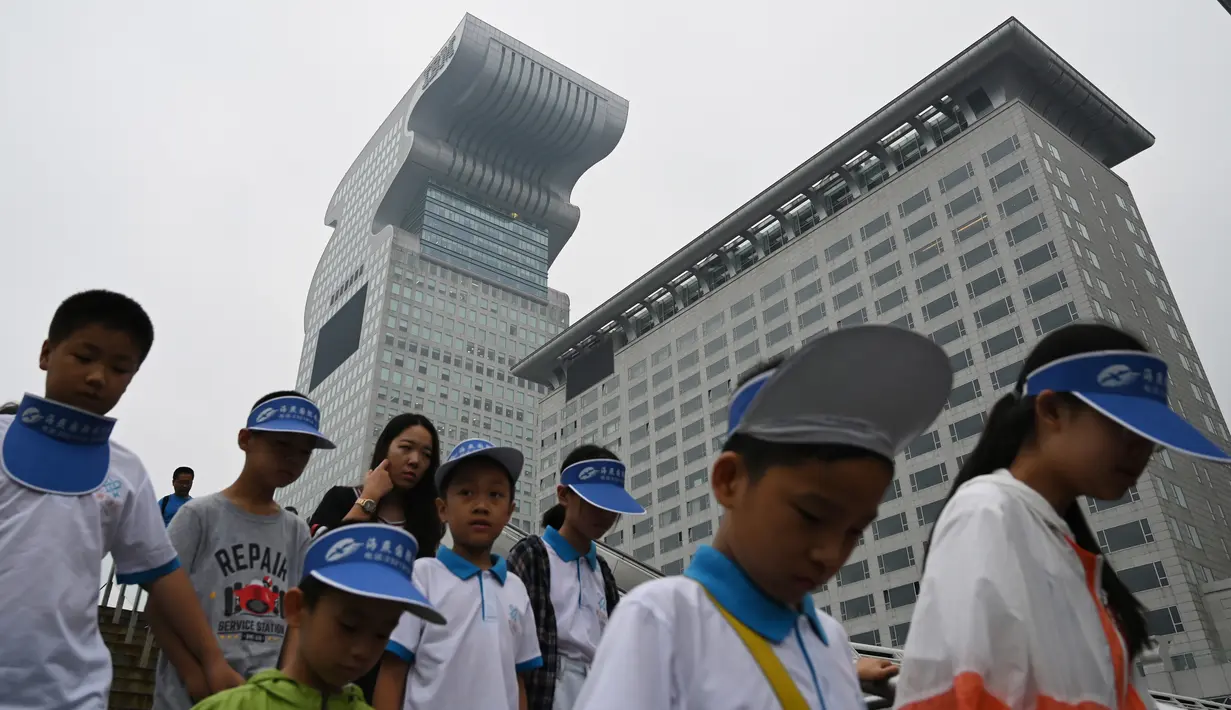 Anak-anak melewati gedung pencakar langit Pangu Plaza di seberang Stadion Olimpiade Bird's Nest, Beijing, Selasa (20/7/2019). Gedung yang pernah masuk dalam film Transformers: Age of Extinction itu terjual dalam lelang online dengan harga 734 juta USD atau sekitar Rp10,5 triliun. (GREG BAKER/AFP)