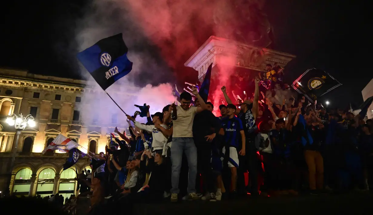Di bawah guyuran hujan gerimis, pendukung Inter Milan tetap berkumpul hingga dini hari untuk menyalakan suar (flares) dan menyanyikan yel-yel kemenangan di bawah ikon katedral Duomo. Tampak dalam foto, para pendukung Inter Milan merayakan gelar juara Serie A musim 2025/2026 atau scudetto ke-21 di Piazza Duomo, Milan, Italia, Minggu (3/4/2026) malam waktu setempat atau Senin (4/5/2026) dini hari WIB. (PIERO CRUCIATTI/AFP)