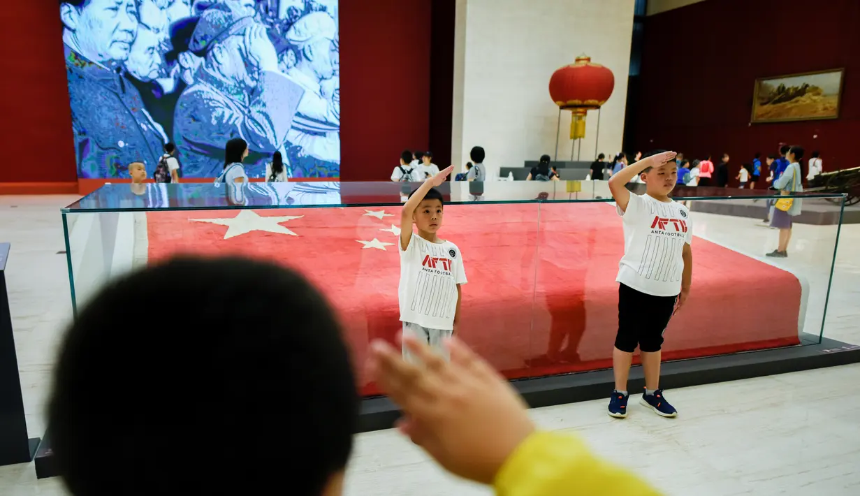 Anak-anak memberi hormat ketika mereka berpose di depan bendera nasional Tiongkok yang dikibarkan pada 1 Oktober 1949 di Museum Nasional China di Beijing (22/8/2019). Tujuan museum ini adalah untuk edukasi mengenai seni dan sejarah Tiongkok. (AFP Photo/Wang Zhao)