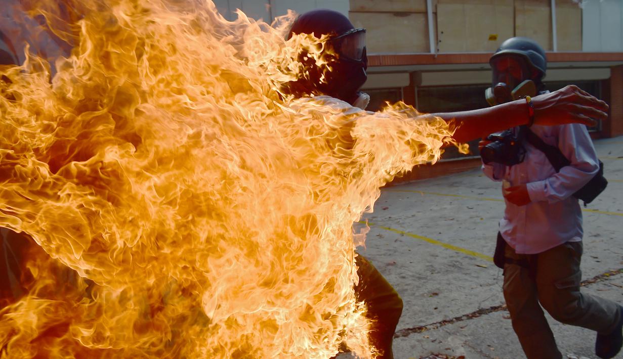 Seorang demonstran berlari saat tubuhnya terbakar disela unjuk rasa yang diwarnai bentrokan menentang Presiden Venezuela, Nicolas Maduro di Caracas, Rabu (3/5). Pria itu tersulut api dari ledakan tangki sepeda motor milik polisi. (RONALDO SCHEMIDT / AFP)