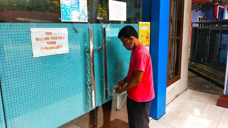 Seorang pria menggembok pintu masuk kantor Camat Bukitraya karena tiga pegawainya positif Covid-19.