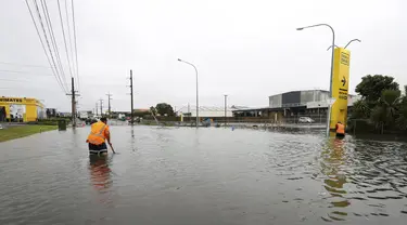 Para pekerja mencoba mensurvei tanah di bawah air banjir di Auckland, Selandia Baru, Rabu (1/2/2023). Peringatan hujan lebat untuk Auckland dicabut, meskipun keadaan darurat tetap berlaku untuk kota terbesar di negara itu setelah curah hujan dan banjir yang mencapai rekor. pada hari Jumat menewaskan empat orang dan menyebabkan gangguan yang meluas. (Brett Phibbs/New Zealand Herald via AP)