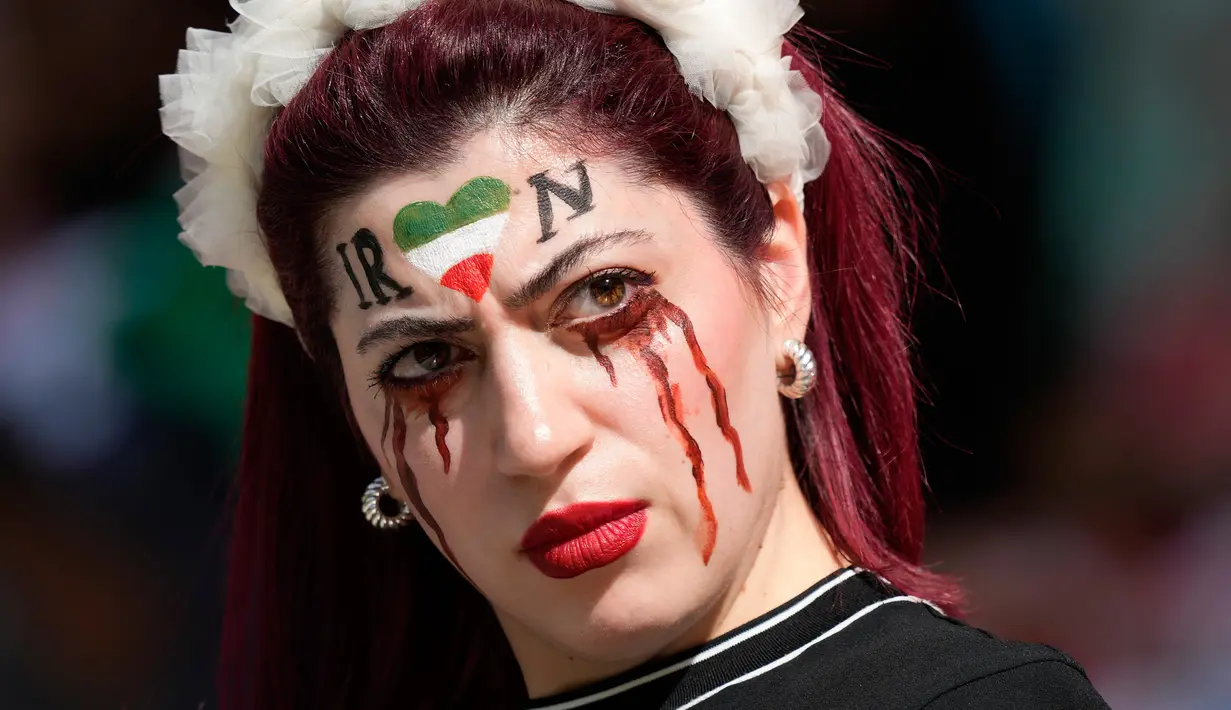 Seorang wanita berdiri di tribun dengan wajah dicat untuk mengenang Mahsa Amini, seorang wanita yang meninggal saat berada dalam tahanan polisi di Iran pada usia 22 tahun, sebelum pertandingan sepak bola Grup B Piala Dunia 2022 antara Wales dan Iran di Ahmad Bin Ali Stadium, Al Rayyan, Qatar, Jumat (25/11/2022). (AP Photo/Frank Augstein)