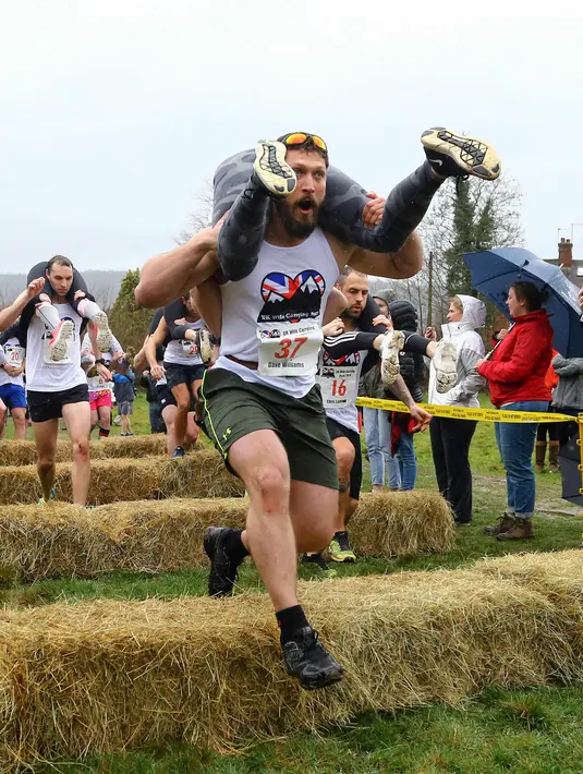 Para peserta melewati rintangan saat Lomba Lari Gendong Istri di The Nower, Dorking, Inggris, Minggu (3/3). Lomba ini digelar setiap tahun di Inggris. (Gareth Fuller/PA via AP)