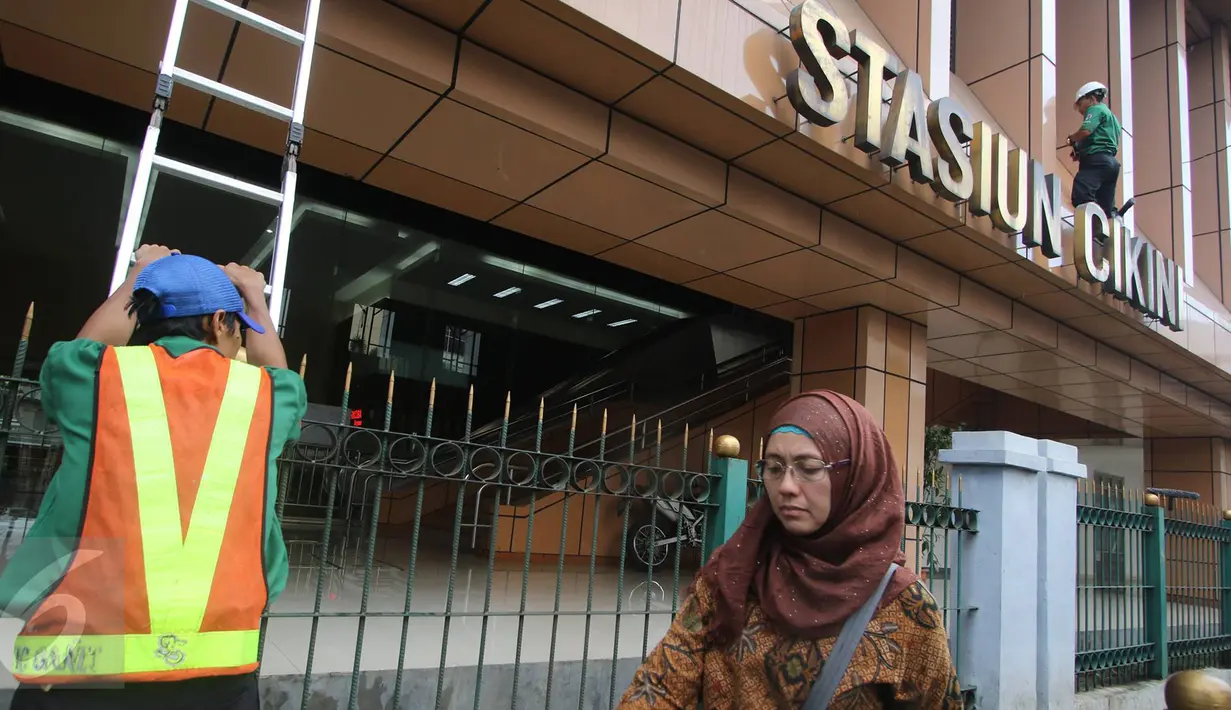 Pengguna jalan melintas di dekat pekerja yang sedang membersihkan dinding Stasiun Cikini di Jakarta, Senin (20/3). (Liputan.com/Immanuel Antonius)