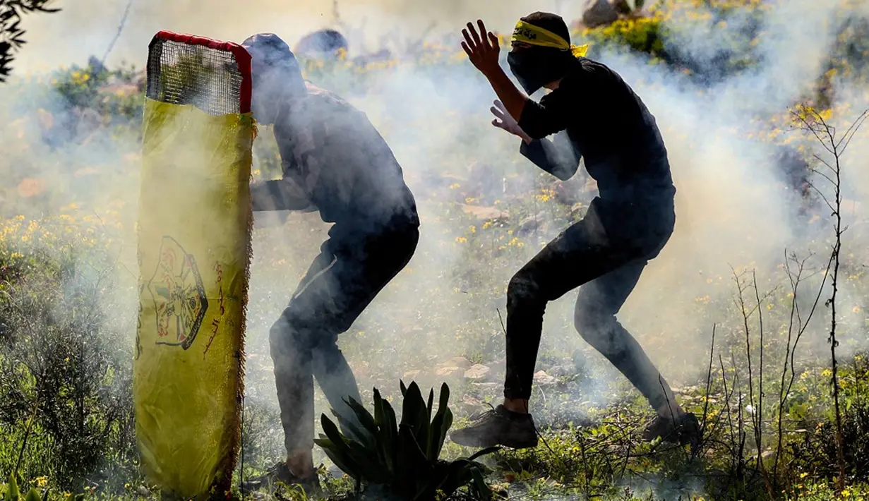 Pemuda Palestina bersembunyi di balik perisai darurat saat bentrok dengan pasukan keamanan Israel pada demonstrasi menentang pengambilalihan tanah oleh Israel dekat pemukiman Yahudi Kedumim di Desa Kfar Qaddum, Tepi Barat, 21 Januari 2022. (JAAFAR ASHTIYEH/AFP)