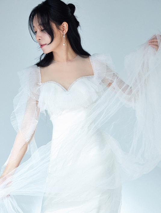 <p>Ia tampak feminin dengan gaun pengantin warna putih. Ia tampak ayu dalam gaun pertama yang memiliki detail ruffle, maupun brukat. (Foto: IOK Company via Soompi)</p>