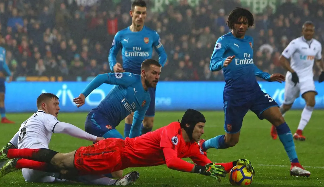 Kiper Arsenal, Petr Cech berusaha menangkap bola yang ditendang pemain Swansea City dalam laga pekan ke-25 Premier League  di Liberty Stadium, Selasa (30/1). Arsenal secara mengejutkan takluk dari Swansea City 1-3. (Geoff CADDICK / AFP)