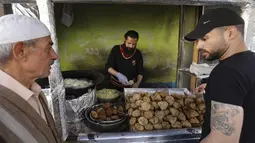 Pelanggan menunggu saat pedagang membuat falafel untuk hidangan berbuka puasa, selama bulan suci Ramadhan di pusat kota Hebron di Tepi Barat yang diduduki (9/4/2022). Makanan ini dibuat dari kacang Arab yang digiling dan kemudian dipadatkan dan dibuat bola-bola kecil lalu digoreng. (AFP/Hazem Bader)