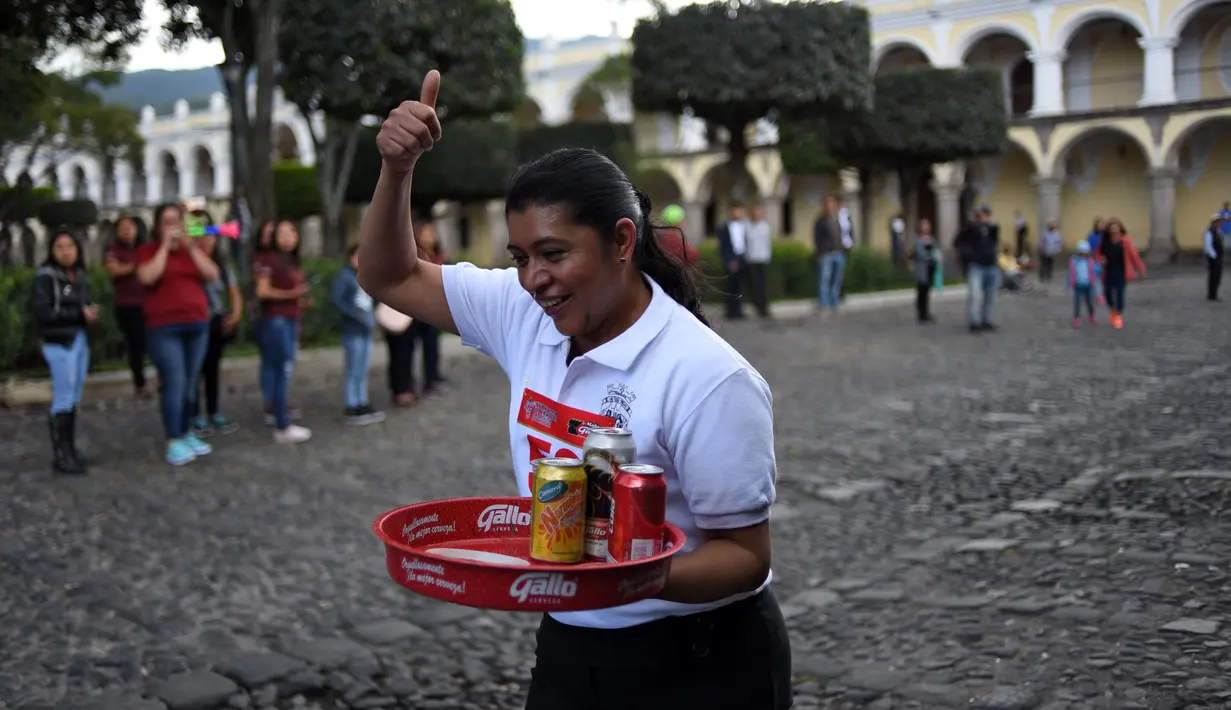 Seorang pramusaji mengacungkan jempol saat mengikuti Waiters Race ke-16 di Antigua, barat daya Ibu Kota Guatemala City, Rabu (14/11). Peserta diminta unjuk kebolehan menggunakan satu tangan membawa nampan berisi minuman. (JOHAN ORDONEZ/AFP)