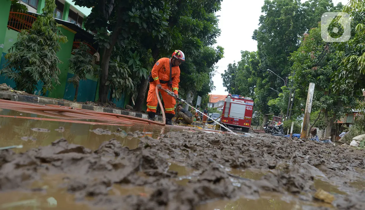 Petugas pemadam kebakaran membersihkan sisa lumpur pascabanjir yang merendam kawasan Bukit Duri, Jakarta, Sabtu (4/1/2020). Meski banjir sudah mulai surut, jalan-jalan dan permukiman warga masih tertutup lumpur tebal. (merdeka.com/Imam Buhori)