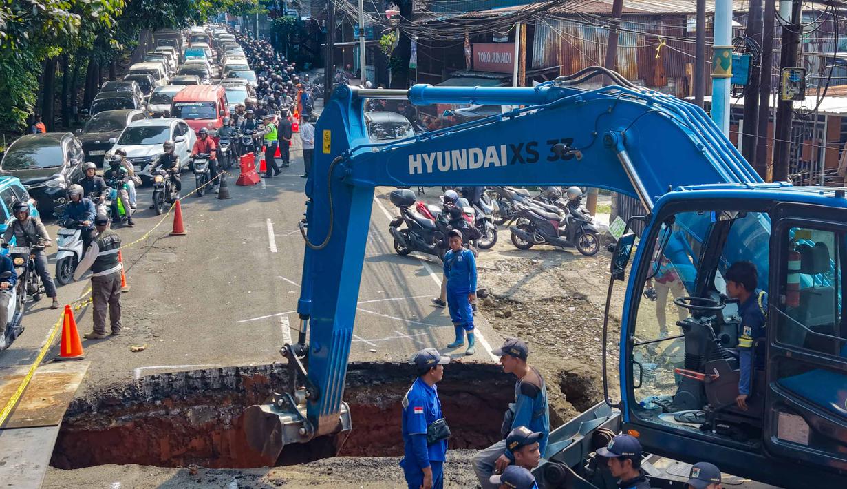 Para pengendara melintas di jalan yang padat sementara para pekerja menggunakan alat berat membersihkan puing-puing dari lubang runtuhan yang terbentuk di Jalan Raya Lenteng Agung (arah Depok), Jakarta pada Jumat 29 Mei 2026. (BAY ISMOYO/AFP)