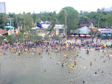 Ribuan pengunjung berenang di Pantai Ancol, Jakarta, Sabtu (26/15). Memasuki libur Tahun Baru sejumlah warga memadati tempat rekreasi di kawasan Ibukota tersebut. (Liputan6.com/Gempur M Surya)