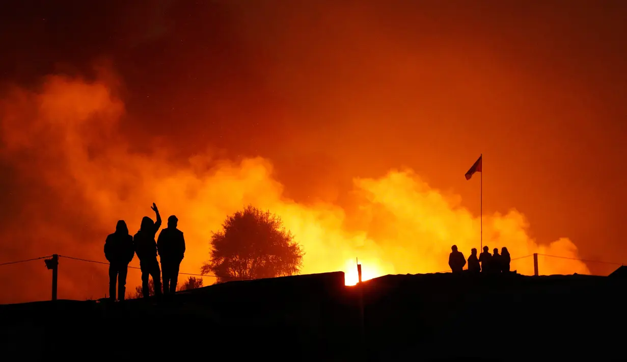 Para imigran melihat tempat penampungan darurat yang terbakar di kamp pengungsian "Jungle" di Calais, Prancis, (26/10). Karena kumuh pemerintah Prancis akhirnya mulai mengosongkan kamp pengungsian imigran tersebut. (REUTERS/Philippe Wojazer)