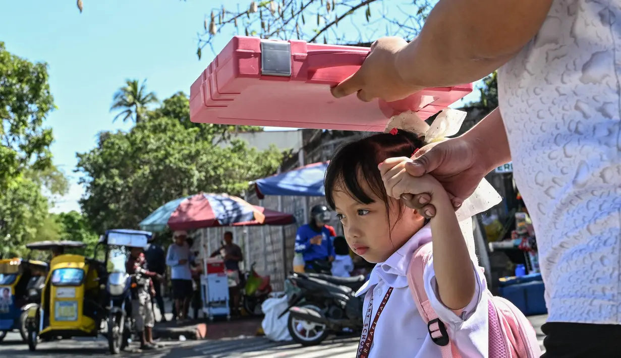 Seorang pria menggunakan tas sekolah untuk melindungi seorang anak dari sengatan matahari saat mereka meninggalkan sekolah di Manila, Filipina pada Senin 3 Maret 2025. (Jam STA ROSA/AFP)