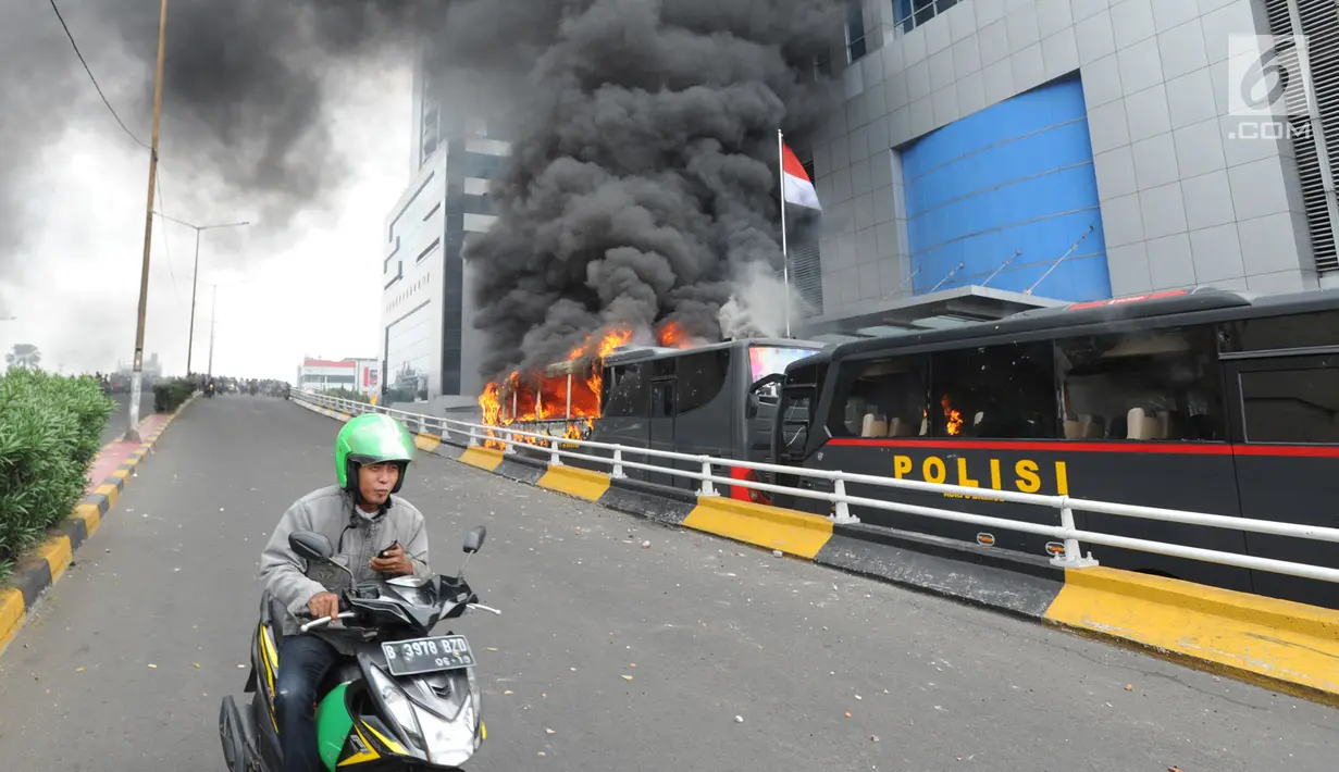 Pengendara ojek online melintasi bus polisi yang terbakar di dekat Flyover Slipi, Palmerah, Jakarta Barat, Rabu (22/5/2019). Belum diketahui penyebab terbakarnya dua bus yang terparkir bersama bus polisi lainnya dilokasi tersebut. (merdeka.com/Arie Basuki)