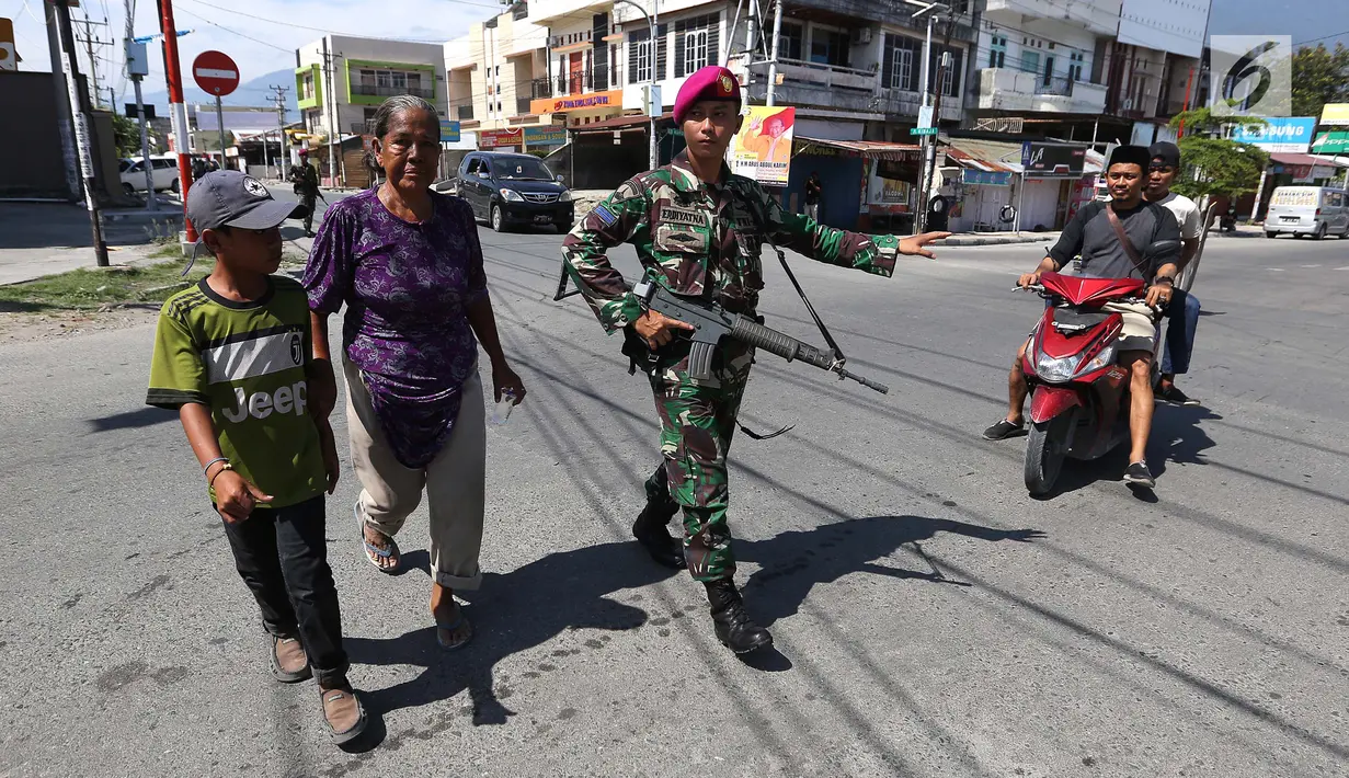 Prajurit Marinir TNI AL membantu warga menyeberangi jalan di perempatan lampu merah kota Palu pascagempa dan tsunami di Palu, Sulawesi Tengah, Jumat (5/10). Selain berjaga di jalan, mereka juga berjaga di beberapa ruko di Palu. (Liputan6.com/Fery Pradolo)