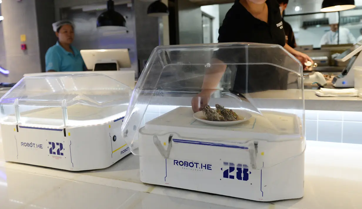 Pekerja meletakkan makanan di robot pelayan restoran Robot.He milik Alibaba di Shanghai, 30 Juli 2018. Tugas robot itu mengangkat tutup kaca hidangan bergaya Shanghai dan mengucapkan, "Selamat menikmati hidanganmu". (AFP)