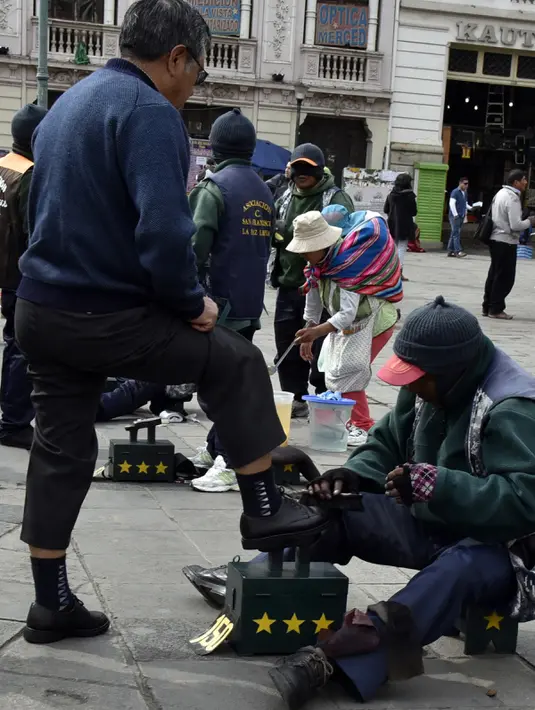 Tukang semir sepatu bertopeng melayani pelanggannya di kawasan La Paz, Bolivia (29/11). Dengan menutup wajahnya para tukang semir ini menyembunyikan identitas karena pekerjaan tersebut dipandang rendah oleh masyarakat lokal. (AFP PHOTO/Aizar Raldes)
