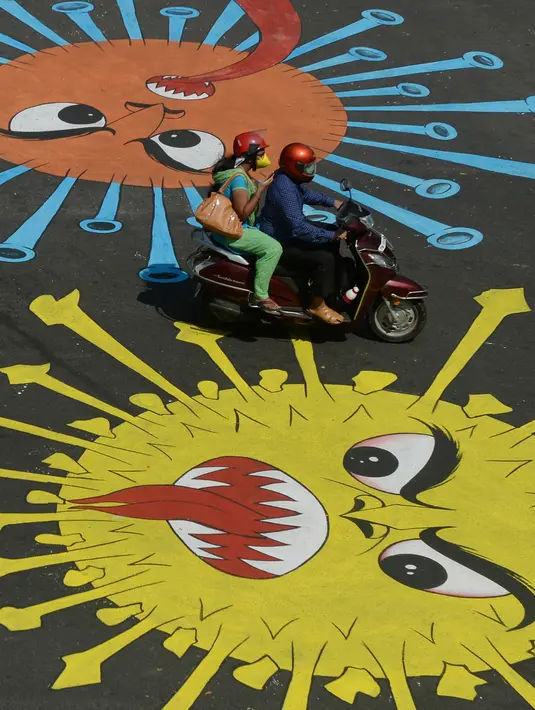 Pengendara motor melewati melewati grafiti virus corona yang dilukis di jalan selama penerapan lockdown nasional di Chennai, India, Senin (13/4/2020). Grafiti itu dibuat untuk meningkatkan kesadaran warga yang keluyuran keluar rumah saat lockdown karena pandemi virus corona. (Arun SANKAR/AFP)