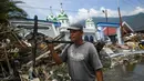 Warga membawa kipas angin yang diselamatkan dari sebuah pasar yang runtuh setelah gempa dan tsunami di  Palu, Kamis (4/10). BNPB menyebut, hingga Kamis sore, jumlah korban meninggal akibat gempa dan tsunami Palu mencapai 1.558 orang. (AFP/Jewel SAMAD)