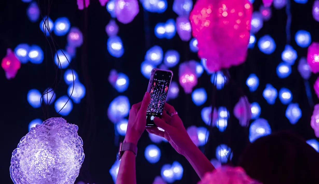 Seorang wanita mengambil foto "Pixel Forest" oleh seniman Swiss Pipilotti Rist, instalasi seni dari 3000 lampu LED pahatan tangan yang digantung di langit-langit di Tai Kwun di Hong Kong (18/8/2022). (AFP/Isaac Lawrence)