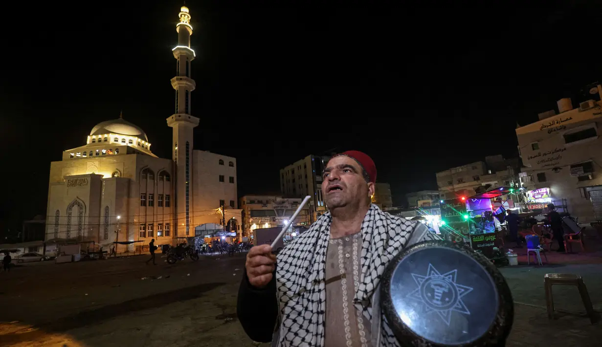 Nizar al-Dabbas Palestina berusia lima puluh tahun, seorang "Musaharati" yang memainkan peran tradisional sebagai "penabuh drum Ramadhan", membangunkan umat Islam untuk makan sahur sebelum fajar selama bulan suci Ramadhan di Khan Yunis di Jalur Gaza selatan (5/4/2022). (AFP/Said Khatib)