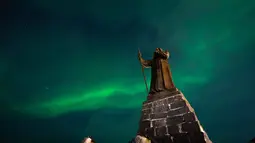Fenomena yang menciptakan pemandangan alam yang memukau ini adalah Aurora Borealis atau cahaya utara. Tampak dalam foto, Aurora Borealis menerangi langit malam di atas patung Hans Egede yang menghadap Nuuk, Greenland, pada 23 Januari 2026. (Jonathan NACKSTRAND/AFP)