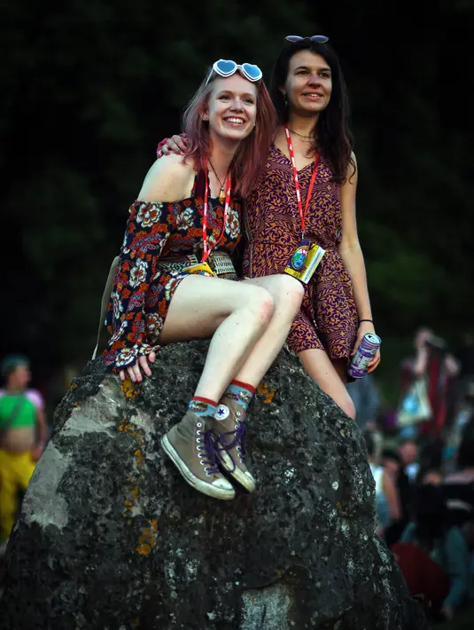 Dua wanita tersenyum saat menghadiri festival Glastonbury dekat desa Pilton di Somerset, Inggris barat daya (22/6/2022). Lebih dari 200.000 penggemar musik dan megabintang Paul McCartney, Billie Eilish, dan Kendrick Lamar turun ke pedesaan Inggris minggu ini saat Festival Glastonbury kembali setelah jeda tiga tahun. (AFP/Andy Buchanan)