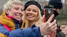 Pamela Anderson berselfie dengan relawan di pengungsian Grande-Synthe, Prancis (25/1). Pamela Anderson adalah seorang aktris yang terkenal berkat filmnya yang menceritakan penjaga pantai yang berjudul baywatch. (AFP/Philippe Huguen)