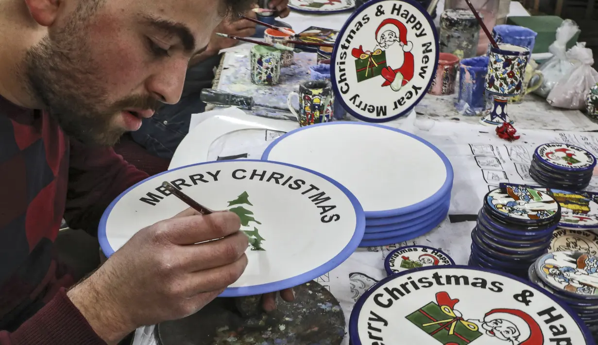 Pekerja Palestina menggambar hiasan bertema Natal di atas piring keramik di sebuah pabrik keramik di kota titik nyala Hebron di Tepi Barat (17/12/2019). (AFP/Hazem Bader)