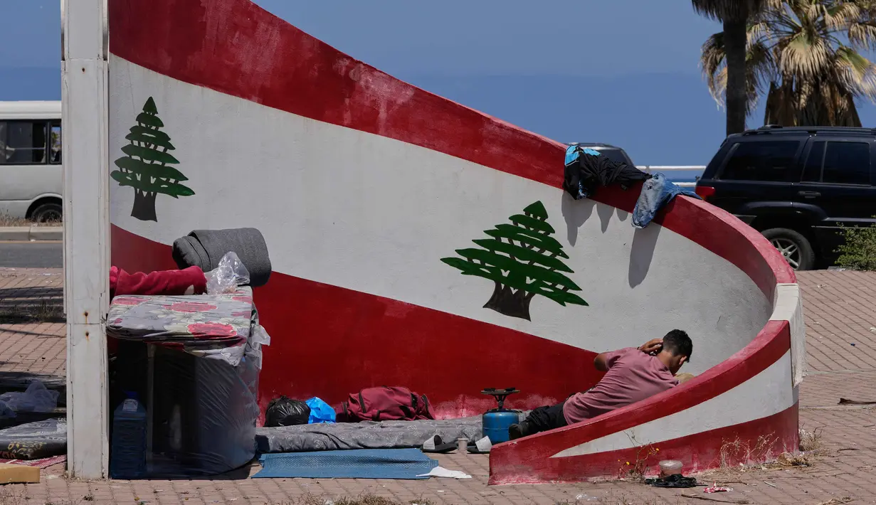 Seorang pengungsi yang meninggalkan desanya di Lebanon Selatan, tergeletak di samping barang-barangnya di trotoar kota pelabuhan selatan Sidon, Rabu 10 Juni 2026. (AP Photo/Mohammed Zaatari)